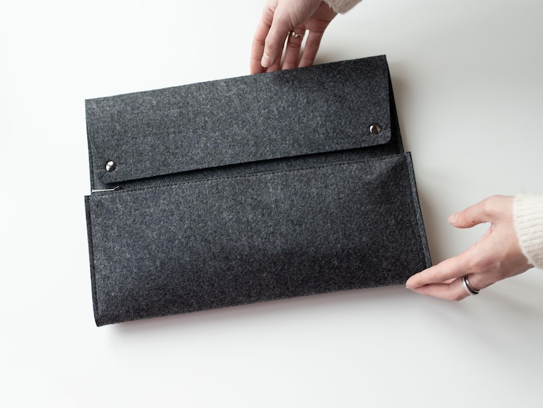 May include: A gray felt zippered pouch with a flap closure and two silver snaps. The pouch is open and being held by a hand.
