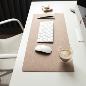 May include: A white desk with a brown felt desk mat, a white keyboard, a white mouse, a cup of coffee, and a white computer monitor.