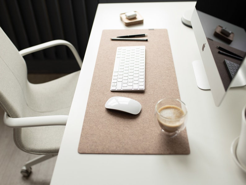 May include: A white desk with a brown felt desk mat, a white keyboard, a white mouse, a cup of coffee, and a white computer monitor.