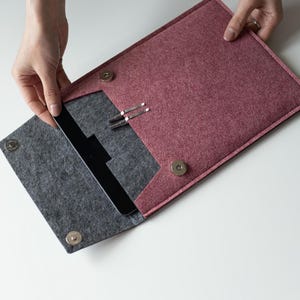 May include: A felt tablet sleeve in a dusty rose color, with a gray interior. The sleeve has a magnetic closure and holds a black tablet. Two silver paper clips are visible inside the sleeve.