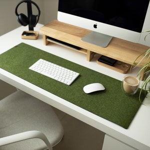 May include: A green felt desk mat with a white keyboard, a white mouse, and a glass of coffee on a white desk.