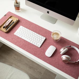 May include: A pink felt desk mat with a white keyboard, a white mouse, a glass of coffee, and rose gold headphones.