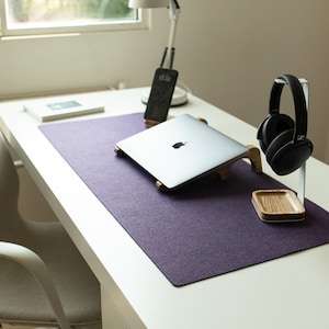 May include: A purple desk mat with a laptop, headphones, and a phone on it. The desk mat is on a white desk.