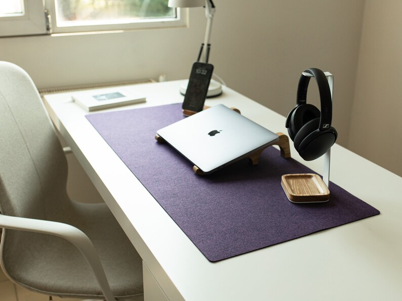 May include: A purple desk mat with a laptop, headphones, and a phone on it. The desk mat is on a white desk.