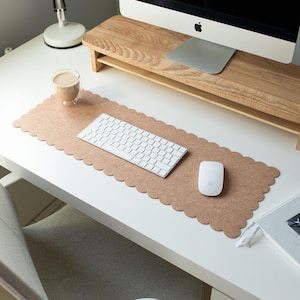 May include: A light brown cork desk mat with scalloped edges. A white keyboard and a white mouse are on the mat. A white desk with a wooden monitor stand is in the background. The text "do it for" is visible on a book.