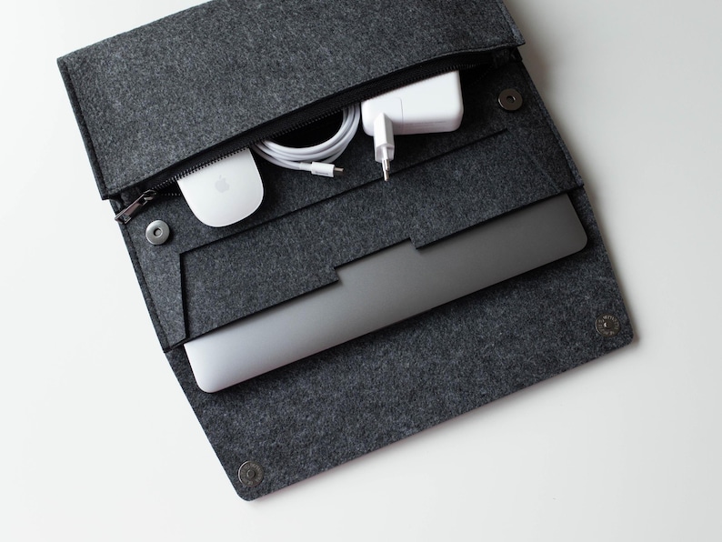 May include: A gray felt laptop sleeve with a zipper closure and a built-in pocket for accessories. The sleeve is open and a laptop, a white wireless mouse, and a white power adapter are visible inside.