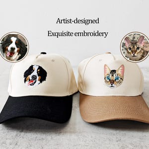 May include: Two baseball caps with embroidered pet portraits. One cap has a black peak and a dog portrait, the other has a tan peak and a cat portrait. The text "Artist-designed Exquisite embroidery" is above the caps.