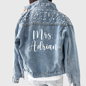 May include: A light blue denim jacket with pearl embellishments on the shoulders and the text "Mrs. Adrian" on the back.