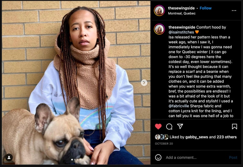 May include: A person wearing a white sweatshirt with a rainbow graphic and a brown fleece neck warmer. The person is holding a light brown French bulldog puppy. The text "Comfort hood by @isainstitches" is visible in the image.