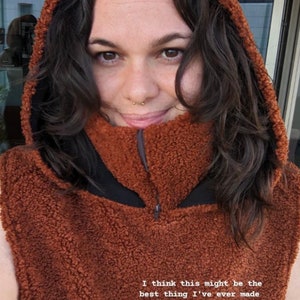 May include: A brown fleece hooded neck warmer with a zip. The text "Look at this #comforthood!!" and "I think this might be the best thing I've ever made @isainstitches" is printed on the neck warmer. The text "CLICK FOR THE HOOD" is printed on a brown button.