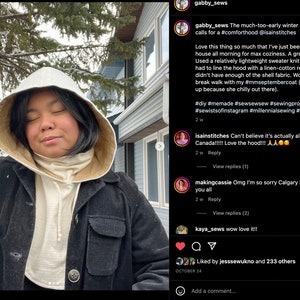 May include: A person wearing a white hooded sweatshirt with a black jacket over it. The person is standing in front of a house with snow on the ground. The caption reads: "The much-too-early winter preview in Calgary calls for a #comforthood @isainstitches"