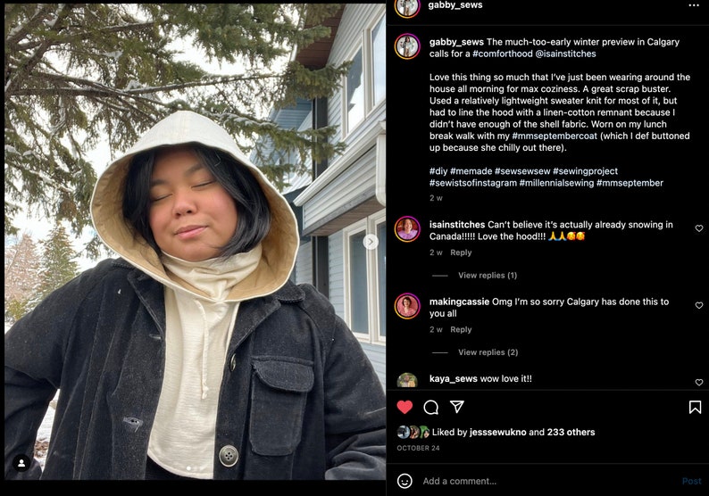 May include: A person wearing a white hooded sweatshirt with a black jacket over it. The person is standing in front of a house with snow on the ground. The caption reads: "The much-too-early winter preview in Calgary calls for a #comforthood @isainstitches"
