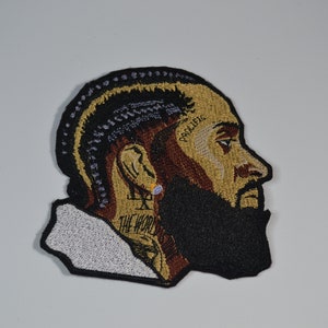 May include: Embroidered patch depicting a side profile portrait with a beard and braided hair. The patch features the word "PROLIFIC" on the forehead and "THE WORLD" on the neck. The patch is black, brown, and tan.