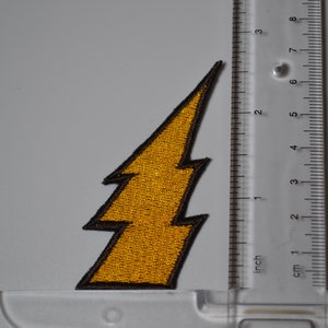 Op de afbeelding: Een gele bliksem-strijkpatch met een zwarte omtrek. De patch is ongeveer 5 cm hoog.