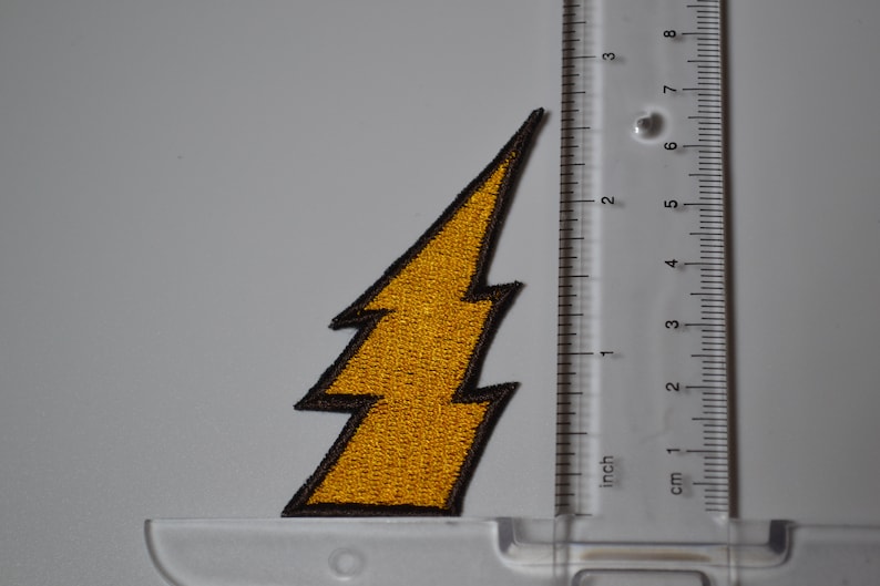 Op de afbeelding: Een gele bliksem-strijkpatch met een zwarte omtrek. De patch is ongeveer 5 cm hoog.