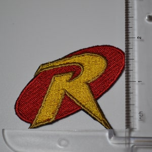 Op de afbeelding: Rode en gele geborduurde strijkpatch met de letter "R" in een gestileerd lettertype. De patch is ongeveer 5 cm breed.