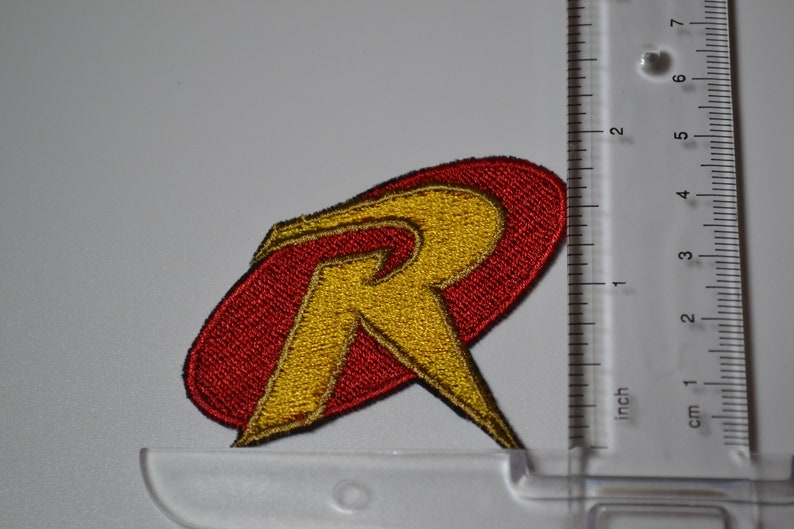 Op de afbeelding: Rode en gele geborduurde strijkpatch met de letter "R" in een gestileerd lettertype. De patch is ongeveer 5 cm breed.