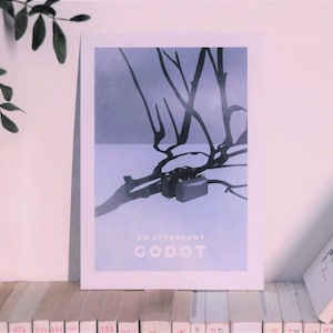 Peut inclure: Une affiche bleue et blanche avec une silhouette noire d'un arbre et deux valises. Le texte "En Attendant Godot" est imprimé en blanc sur l'affiche.