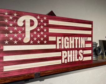 May include: A wooden American flag with a red, white and blue colour scheme. The flag has a white "P" in the top left corner and the words "FIGHTIN' PHILS" in white lettering on the right side of the flag.