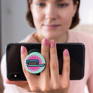 May include: A turquoise blue phone grip with a pink flower design and a cartoon illustration of a toothbrush and toothpaste.