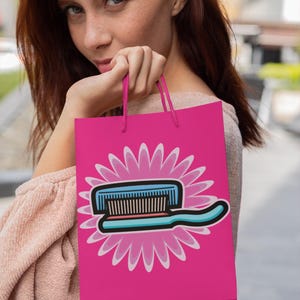 May include: A pink shopping bag with a white and blue toothbrush graphic on a pink flower design. The bag has white handles.