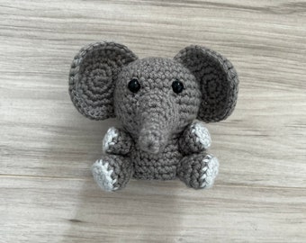 Pode incluir: Um elefante de crochê cinza feito à mão com orelhas grandes, uma longa tromba e pequenos olhos pretos. Os pés do elefante têm detalhes em branco e cinza. Este brinquedo macio é perfeito para um bebê ou criança.