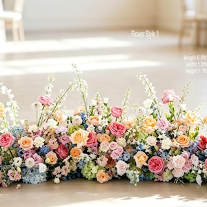May include: A floral arrangement labelled Flower Style 1 with dimensions of 200cm in length, 40cm in width, and 55cm in height, featuring a mix of pink, peach, blue, and white roses, hydrangeas, and tall white delphinium flowers.