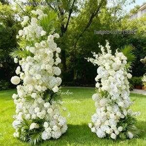 以下が含まれることがあります： 緑の芝生に、高さ200cmと150cmの白いフラワーアレンジメントが2つあります。白いバラ、アジサイ、その他の花々が、緑の葉のアクセントとともに配置されています。「Jackon Customization」の文字が見えます。