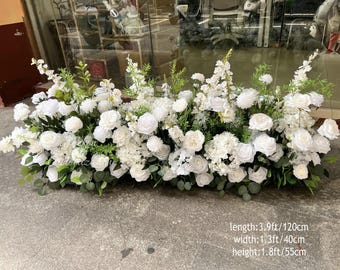 May include: A rectangular floral arrangement featuring white roses, hydrangeas, and other white flowers with green foliage. The arrangement is 3.9 feet long, 1.3 feet wide, and 1.8 feet high.