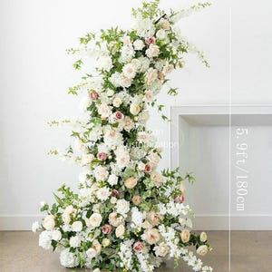 May include: A floral arrangement featuring white and blush roses, greenery, and other flowers. The arrangement is approximately 5.9 feet (180 cm) tall and 2.6 feet (80 cm) wide. The flowers are arranged in an arch shape, suitable for weddings or events.