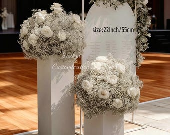 May include: White floral arrangements on square pedestals, with a matching backdrop. The backdrop is decorated with greenery and white flowers. The text on the backdrop says "size: 22inch/55cm".