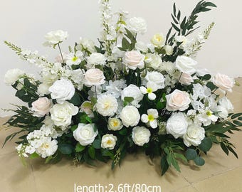 May include: A floral arrangement featuring white and light pink roses, white blossoms, and green foliage. The arrangement is approximately 2.6 feet long, 1.3 feet wide, and 1.8 feet high.