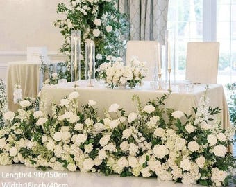 Op de afbeelding: Een prachtig versierde bruiloftstafel met witte bloemen en groen. De tafel is bedekt met een crèmekleurig tafelkleed en heeft een bloemstuk in het midden. De tafel is 150 cm lang, 40 cm breed en 55 cm hoog.