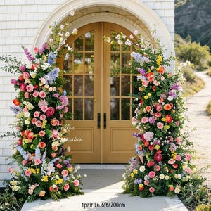Op de afbeelding: Twee bloemstukken omlijsten een houten deur. De arrangementen bestaan uit kleurrijke bloemen, waaronder rozen. De tekst "Jackson Customization" is zichtbaar. De basis van elk arrangement is ongeveer 200 cm.