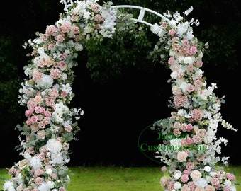 May include: A white metal wedding arch adorned with an abundance of flowers in shades of pink, white, and green. The floral arrangement includes roses, hydrangeas, and eucalyptus leaves, creating a romantic and elegant display for outdoor ceremonies.