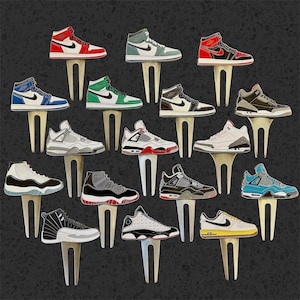 May include: A collection of miniature sneaker figurines in various colorways, including red, blue, green, and black. Each sneaker is mounted on a white stand, showcasing iconic designs and details. The sneakers are arranged on a dark gray background.