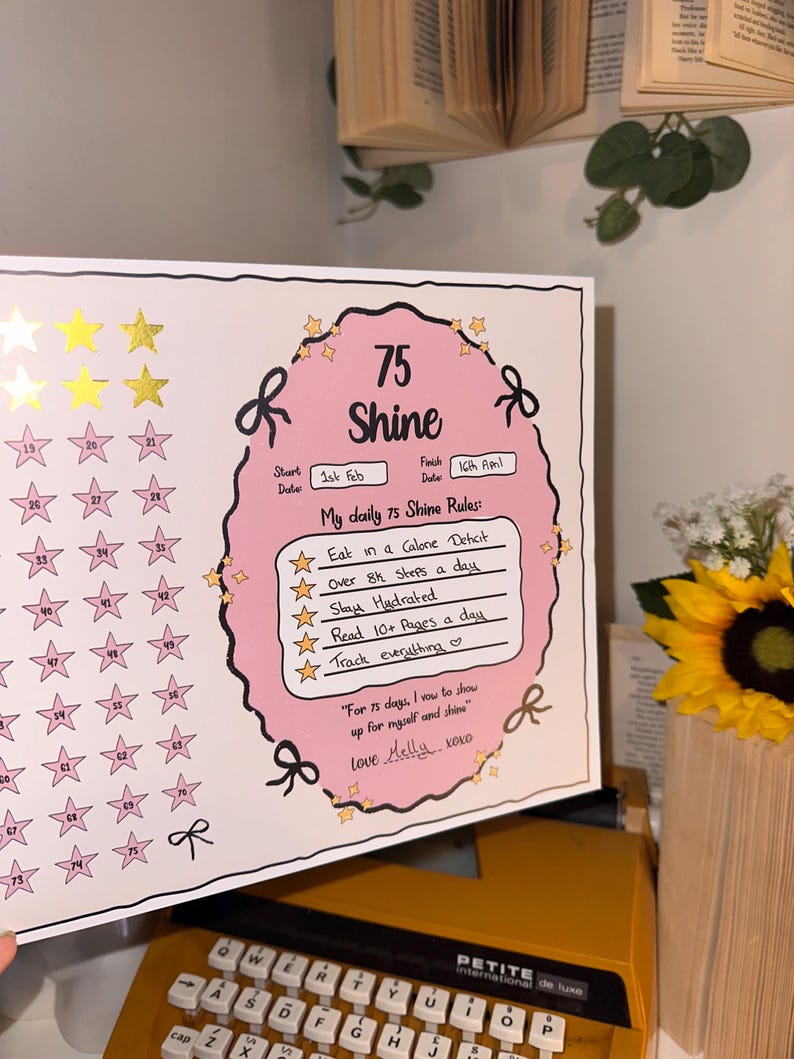 May include: A pink and white 75-day Shine tracker with gold stars and a pink oval in the center. The tracker includes daily rules and a motivational quote. The start date is February 1st, and the finish date is April 16th.