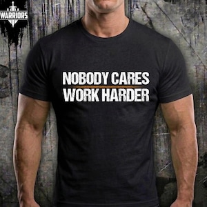 Puede incluir: Una camiseta negra de manga corta con el texto blanco de estilo desgastado "NOBODY CARES" en la línea superior y "WORK HARDER" en la línea inferior, separados por una fina línea horizontal naranja en el centro del pecho.