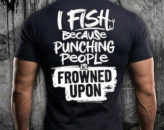 Puede incluir: Una camiseta negra de manga corta con texto blanco en la espalda que dice I FISH BECAUSE PUNCHING PEOPLE IS FROWNED UPON. El diseño incluye un pequeño gráfico de anzuelo y un icono de pez, con las palabras FROWNED UPON dentro de un recuadro blanco.