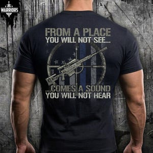 May include: A black short-sleeved t-shirt featuring a graphic on the back. The design includes a sniper rifle over a circular target and a thin blue line flag motif, with the text FROM A PLACE YOU WILL NOT SEE... COMES A SOUND YOU WILL NOT HEAR.