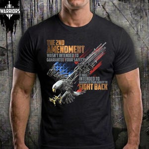 Peut inclure: T-shirt noir avec un aigle et un fusil, et le texte "THE 2ND AMENDMENT WASN'T INTENDED TO GUARANTEE YOUR SAFETY IT WAS INTENDED TO GUARANTEE YOUR ABILITY TO FIGHT BACK". Le t-shirt porte également le logo "WARRIORS".
