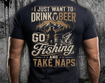 Puede incluir: Una camiseta negra de manga corta con un gráfico en la espalda que incluye el texto I JUST WANT TO DRINK BEER GO FISHING AND TAKE NAPS. El diseño muestra a una persona pescando en un lago con montañas, una jarra de cerveza y un pez.