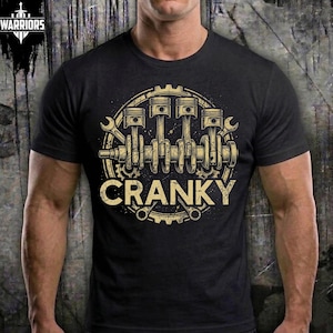May include: Black t-shirt with a gold-colored graphic of engine pistons, crankshaft, and wrenches. The word "CRANKY" is printed in a distressed font within a circular design. The shirt has short sleeves.