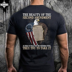 May include: Black t-shirt featuring a graphic of an eagle holding a scroll with the text "THE BEAUTY OF THE SECOND AMENDMENT" and "IS THAT IT WILL NOT BE NEEDED UNTIL THEY TRY TO TAKE IT". The eagle has wings in the colors of the American flag.