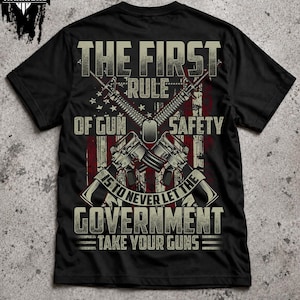 Puede incluir: Una camiseta negra con un estampado gráfico de dos rifles cruzados sobre una bandera estadounidense desgastada. El texto dice: THE FIRST RULE OF GUN SAFETY IS TO NEVER LET THE GOVERNMENT TAKE YOUR GUNS. Una placa de identificación militar está centrada.