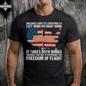 May include: Black t-shirt with the text "AN EAGLE CAN'T FLY WITH ONLY A LEFT WING OR RIGHT WING." The shirt features a graphic of the United States flag with a bandage over it. The text "IT TAKES BOTH WINGS WORKING TOGETHER TO EXPERIENCE THE FREEDOM OF FLIGHT" is also printed on the shirt.