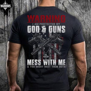 Peut inclure: Un t-shirt noir à manches courtes avec une impression graphique au dos. Le texte indique WARNING I AM PROTECTED BY GOD & GUNS MESS WITH ME & YOU MIGHT MEET THEM BOTH. Le motif montre deux pistolets croisés et un chapelet sur un drapeau.