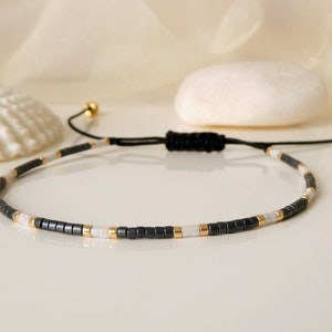 Armband aus Miyuki Delica Perlen in anthrazit, weiß und gold, verstellbar durch Schiebeknoten, im Geschenktütchen