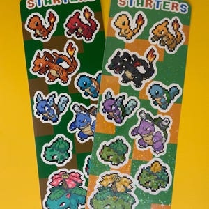 May include: Two rectangular stickers with pixelated images of starter Pokémon. The stickers have a green background with a checkerboard pattern. The word "STARTERS" is printed at the top of each sticker. The Pokémon are in various colors, including orange, blue, and green.