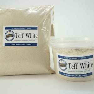 Può includere: Due contenitori di farina di teff bianca, uno in un sacchetto di plastica trasparente e l'altro in un contenitore di plastica trasparente. Entrambi i contenitori hanno un'etichetta che recita "Authentic Ethiopian Spices Teff White" con gli ingredienti elencati come "Teff bianco macinato" e il sito web "EthiopianSpices.com".